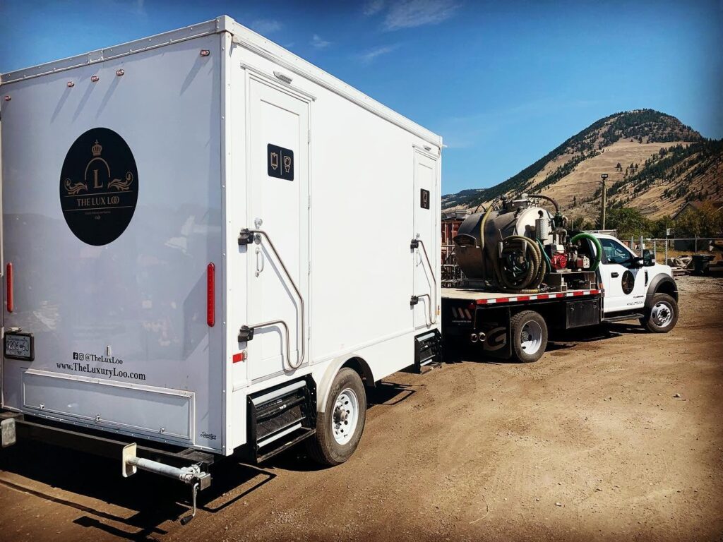 The Lux Loo portable washroom trailer being transported by a pickup truck along a gravel road in BC.